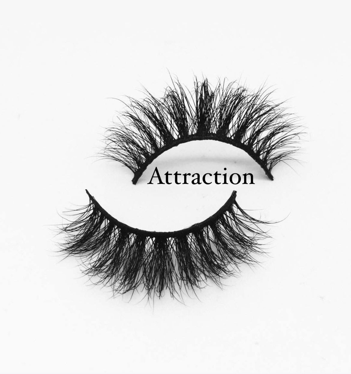 A pair of thick, wispy false eyelashes labeled "MesmerEyes Mink Lashes" is positioned on a white background. One lash is slightly curved upwards, while the other lies below it, curving downwards. These Nayy Seduction Brand lashes are perfect for captivating any audience.